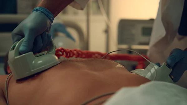 Médico mãos desfibrilando paciente em hospital de emergência perto. — Fotografia de Stock