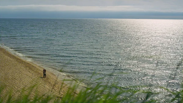 Ζευγάρι στέκεται τοπίο παραλία. Κοντινό γρασίδι φυσάει αέρα στο φόντο της θάλασσας. — Φωτογραφία Αρχείου