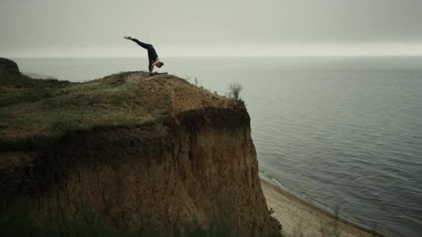 Beautiful woman bending body to foot practicing yoga asana on beach hill. — 비디오