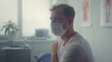 Tired patient sitting wearing mask in clinic closeup. Man waiting physician.