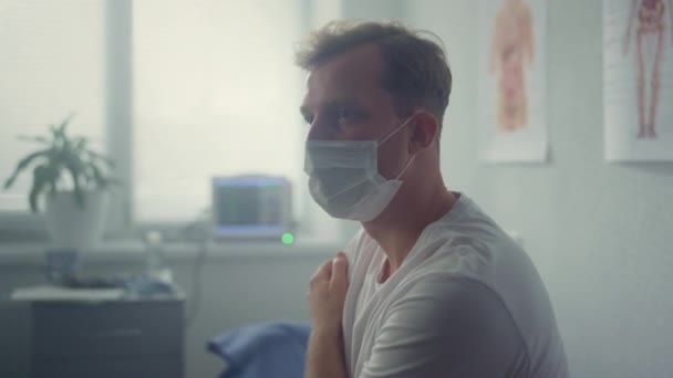 Trött patient sitter bär mask på kliniken närbild. Man väntar läkare. — Stockvideo