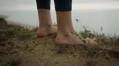 Barefoot unknown woman standing beach hill close up. Bare legs placed hilltop.