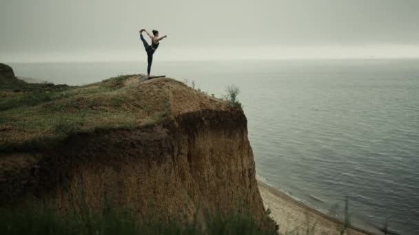 Athlete woman streching holding leg on beach hill. Girl practicing yoga near sea — Stock video