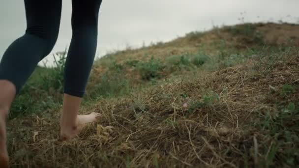 Onbekende vrouwenvoeten lopen de groene heuvel op van dichtbij. Meisje klimt op heuveltop. — Stockvideo