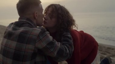 Gün doğumunda sahilde öpüşen romantik bir çift. Kız ve erkek birbirlerine sarılıyorlar.