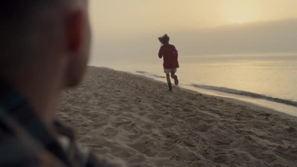 Giovane coppia trascorrere le vacanze sulla spiaggia all'alba. Uomo seduto sulla riva dell'oceano — Video Stock