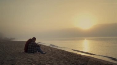 Loving couple sitting on sandy beach at ocean. Young lovers talking together