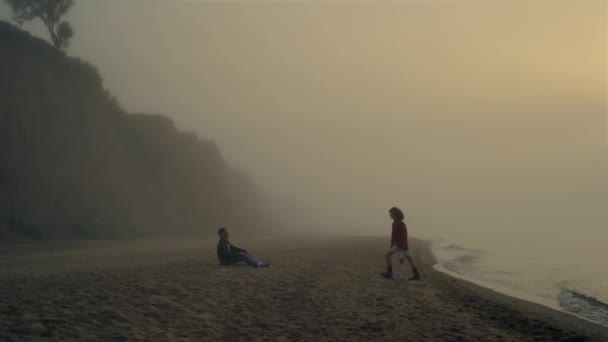 Young couple relaxing on beach at sunrise. Boyfriend and girlfriend kissing — Stockvideo