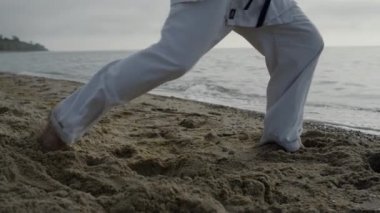 Bilinmeyen adam ayakları kuma karate tekmeleri atıyor. Sahile ayak basan bir sporcu