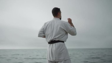 Sporcu deniz kenarında karate antrenmanı yapıyor. İnsan tekniği öğrenir.