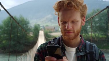Hitchhiker texting mobile phone at mountains. Smiling guy read news outside.