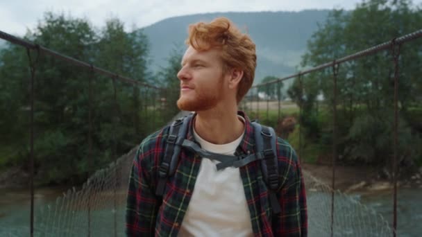 Hiker walking mountain valley bridge. Redhead guy enjoying adventure outside. — Stockvideo