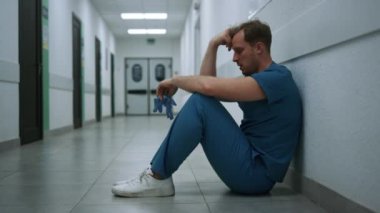 Stresli cerrah ameliyat sonrası klinik koridorunda kalıyor. Doktor yalnız oturuyor..