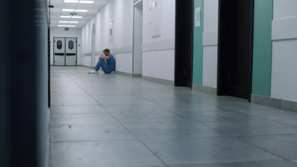 Κουρασμένος γιατρός κάθεται στο διάδρομο του νοσοκομείου. Συγκλονισμένος χειρουργός αναπαύεται μόνος. — Αρχείο Βίντεο