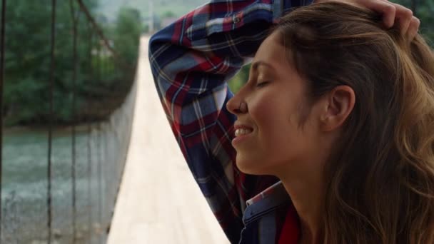 美丽的女人在大自然的河桥上抚摸着头发.在山上远足的旅客. — 图库视频影像