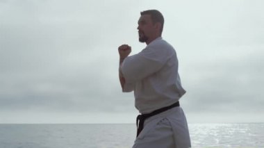 Sahile yakın planda karate yapan odaklanmış bir sporcu. Erkek dövüş teknikleri