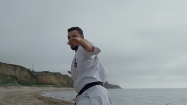 Sportsman practicing hands punches on gloomy beach. Focused man workout karate. — Wideo stockowe