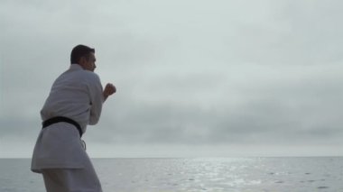 Sporcu deniz kıyısında dövüş sanatları öğreniyor. Sakallı adam dövüş teknikleri çalışıyor.