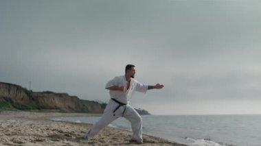 Karate sporcusu güneşli plajda tekme pratiği yapıyor. Sporcu adam dövüş sanatları eğitimi alıyor.