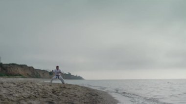 Deniz kıyısında dövüş teknikleri öğrenen bir adam. Atletik dövüşçü karate çalışıyor..