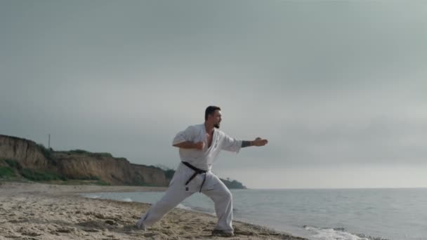 Atleta di karate che pratica calci sulla spiaggia soleggiata. Sport uomo formazione arti marziali — Video Stock