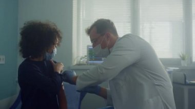 Doktor, reşit olmayan hastaya klinikte aşı yapılması için bağışıklık verdi. Erkek kıza iğne yapıyor..