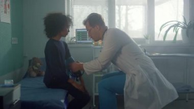 Ergenlik çağındaki çocuk doktoru hastanede ziyaret ediyor. Doktor kız elinin üzerine tonometre koyuyor. 