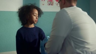 Çocuk doktoru çocuk koluna tonometre kelepçe takıyor. Kız konuşuyor doktor. 