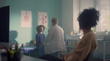 Doctor checking girl visual reflex in office. African mom waiting tests results.