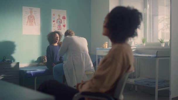 Pediatrician examining girl throat. Mom sitting waiting on medical consultation. — Stockvideo