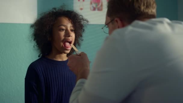Dottore che usa il depressore per controllare la gola della ragazza. Medico guardando in bocca aperta — Video Stock