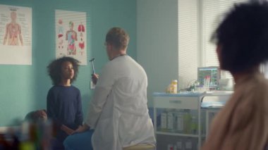 Pediatrician checking preteen girl visual reflex using neurological hammer.