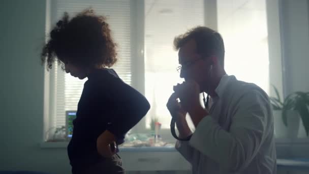 Allvarlig läkare lyssnar andning preteen patient som använder stetoskop på kliniken — Stockvideo