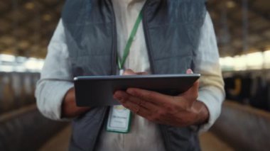 Eller tablet ekranı kapatıyor. Odaklanmış çiftlik hayvanları müdürü ahırda çalışıyor..