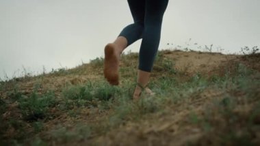 Barefoot girl climbing green hill close up. Young lady feet walking seacoast.