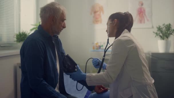 Žena kardiolog měření tlaku senior pacient v nemocnici kancelář detailní záběr — Stock video
