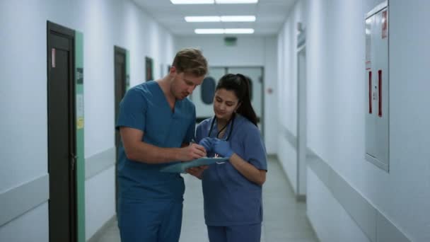 Focused doctor discussing report with medical nurse in hospital corridor. — Stock Video