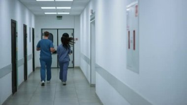 Unknown doctor nurse moving down hallway back view. Surgeon consulting woman.
