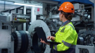 Modern büyük dijital fabrikada çalışan üniformalı uzman dizüstü bilgisayar..