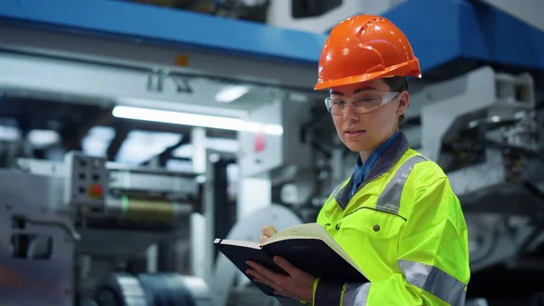 Kobieta pracownik fabryki patrząc aparat w pobliżu dużych konstrukcji produkcji metalu. — Zdjęcie stockowe