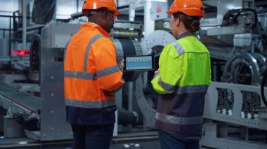 Büyük fabrikadaki modern tablet bilgisayarların grafiklerini tartışan odaklanmış ortaklar..