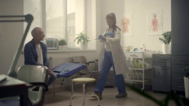 Woman therapist examining senior patient throat. Old man visit doctor in clinic.