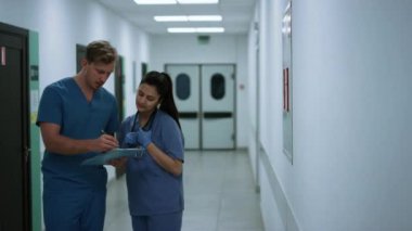 İki doktor klinik koridorunda konuştuktan sonra hastalara yardım ediyor..