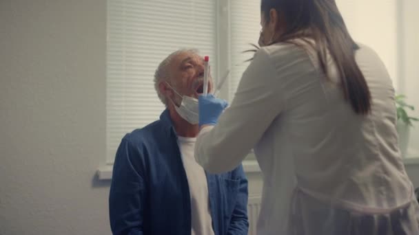 Hombre mayor dando pruebas de saliva en la clínica de cerca. Mujer médico tomando muestra. — Vídeos de Stock