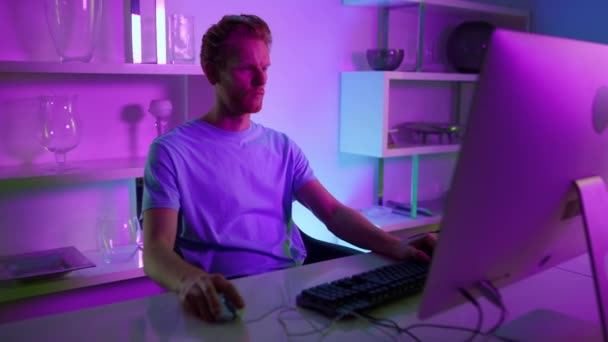 Freelancer working neon lights room. Serious man using pc surfing internet home — 비디오