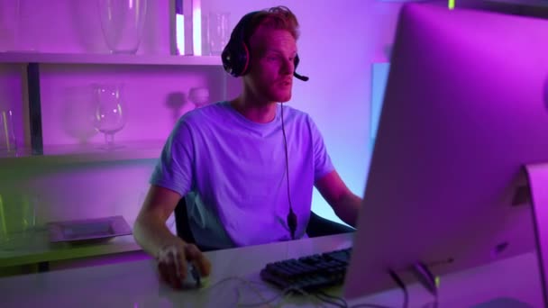 Un uomo in diretta streaming nella stanza al neon. Gioioso giocatore commentando le azioni in cuffia — Video Stock