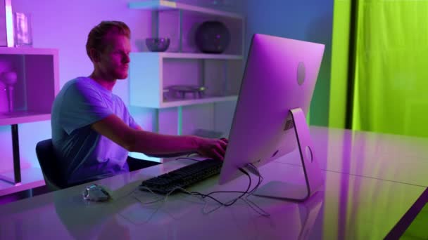 Gamer putting headphones playing computer game at home. Neon lights interior. — Vídeo de Stock