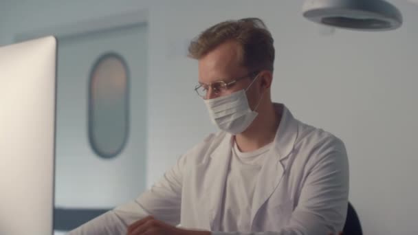 Médico mascarado observando monitor na clínica de perto. Relatório de redação do médico homem — Vídeo de Stock