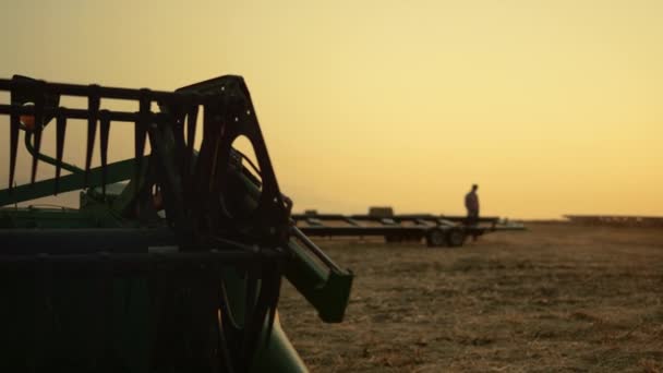 Silhouette dell'agricoltore alle attrezzature per la raccolta dei campi di grano all'ora del tramonto dorato. — Video Stock