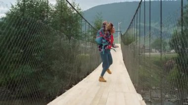 Dağları yöneten mutlu turistler nehir köprüsü. Heyecanlı kız doğaya atlıyor.